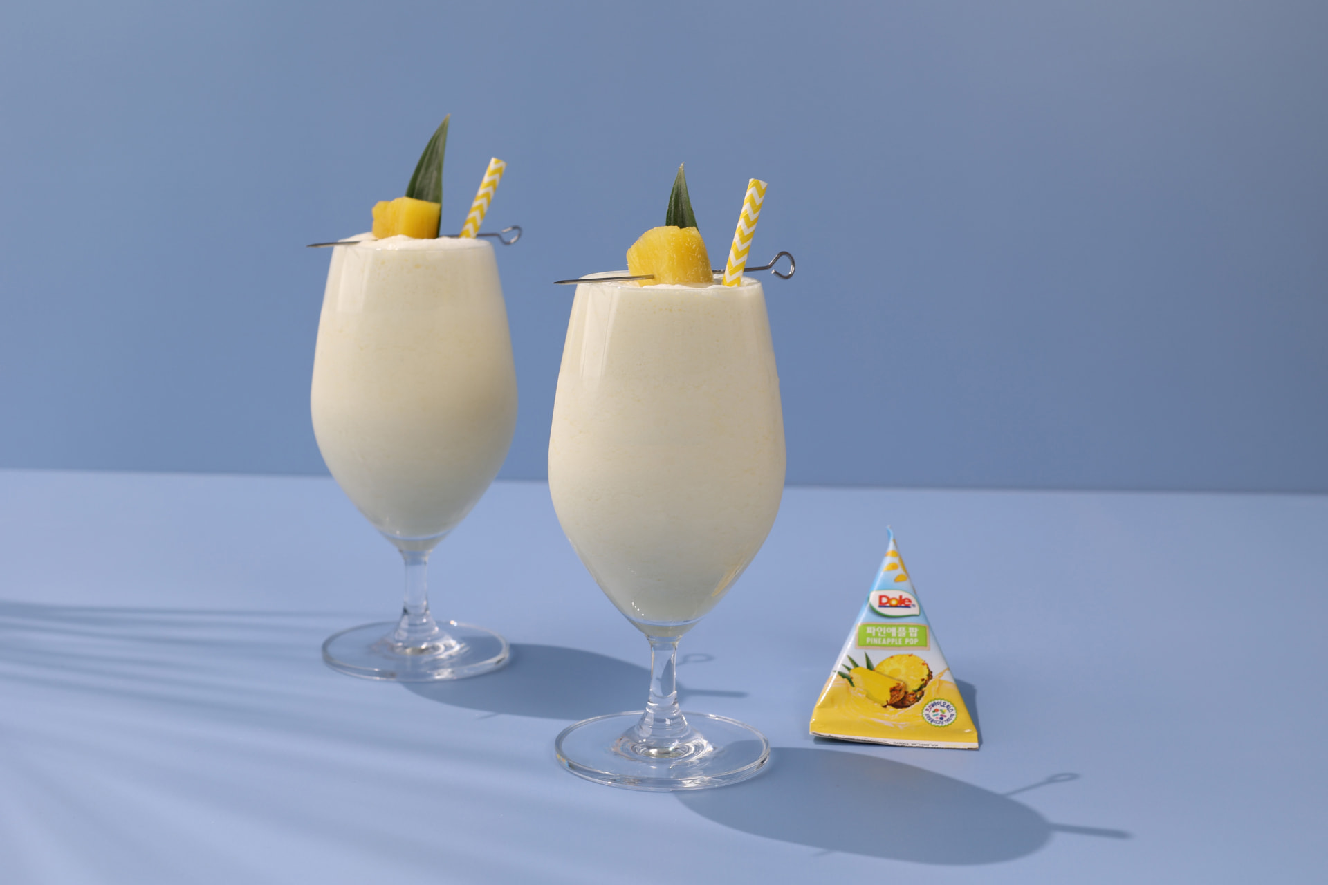 Dole pineapple smoothie glasses styled on a soft blue set